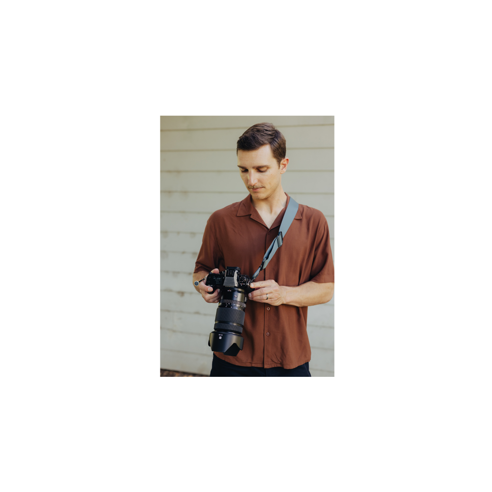 Een man in een bruin shirt houdt een camera met lens vast. Houten muur achtergrond.