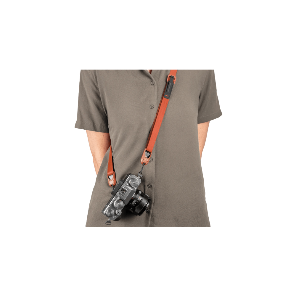 Een persoon draagt een grijs shirt met een oranje camerariem en een zilveren camera.