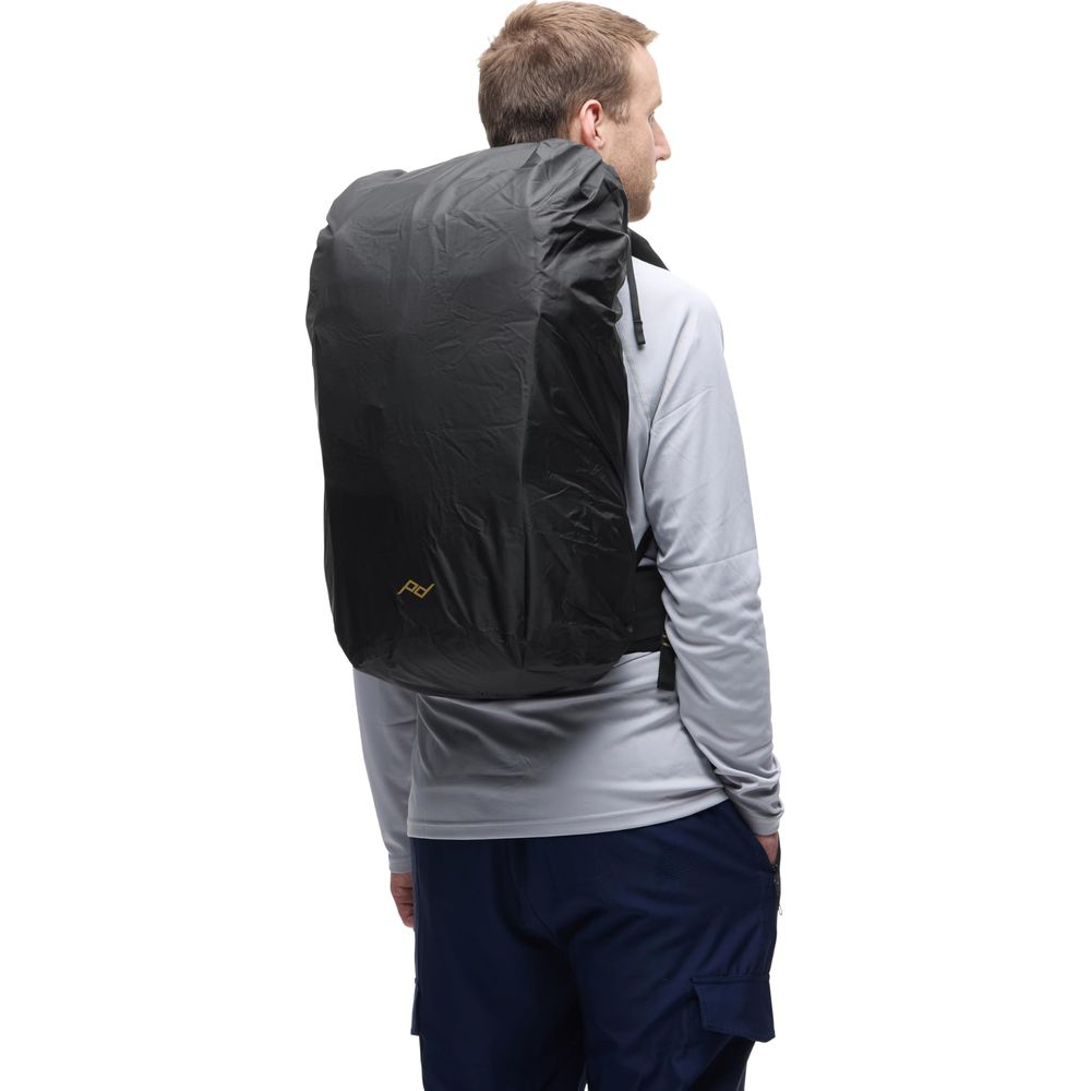 Man met zwarte rugzak met regenhoes, grijs shirt en blauwe broek.