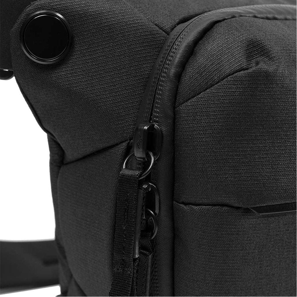 Close-up van een zwarte tas met rits- en riemdetails.