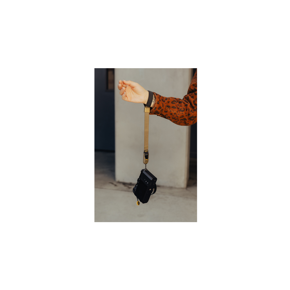 Een hand in een bruin luipaardprint shirt houdt een camera aan een polsband vast.