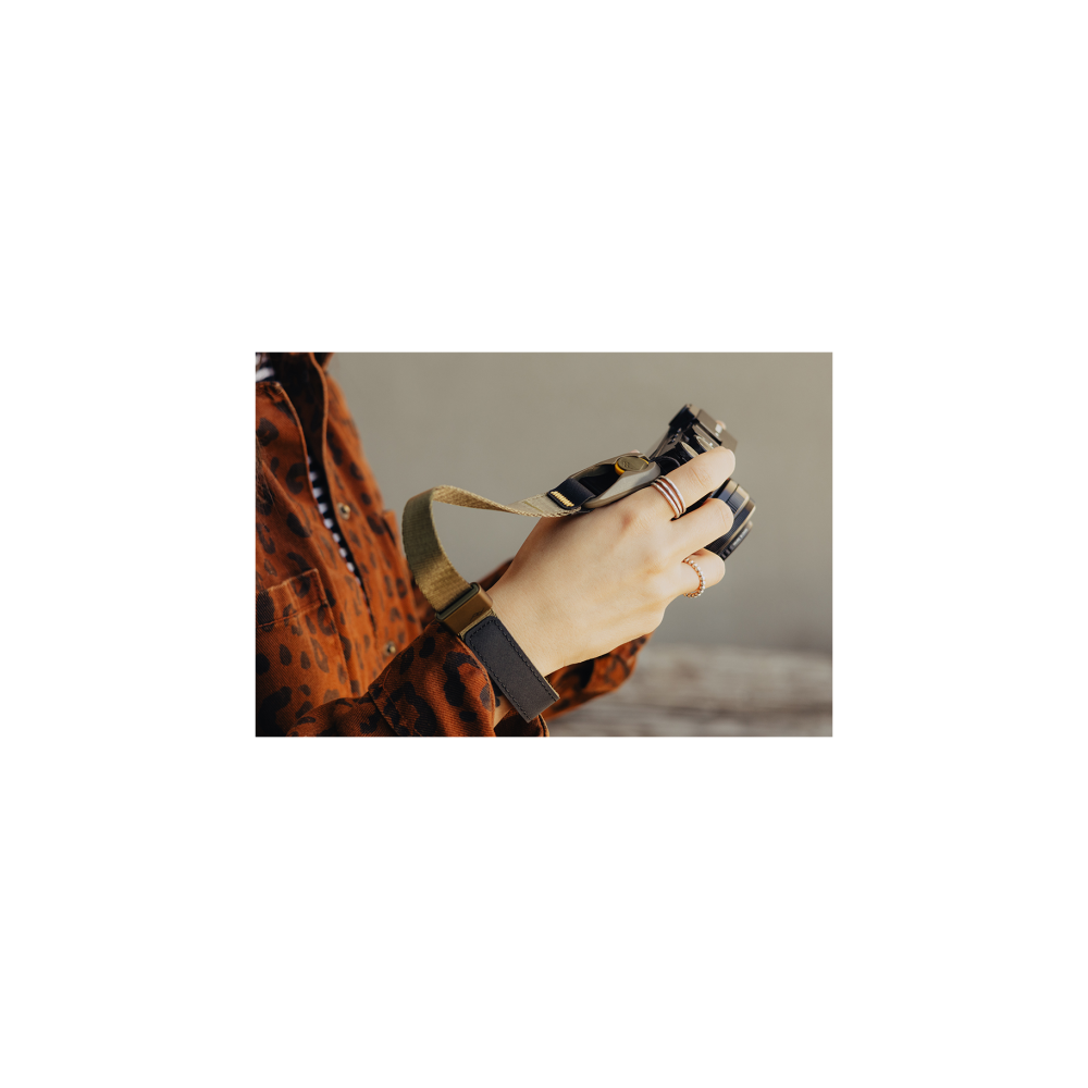 Handen met ringen houden een camera met riem vast.