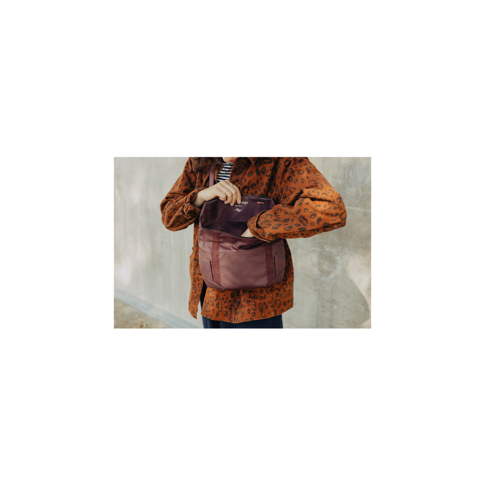 Person in brown leopard jacket opens a burgundy bag. Gray concrete wall in background.