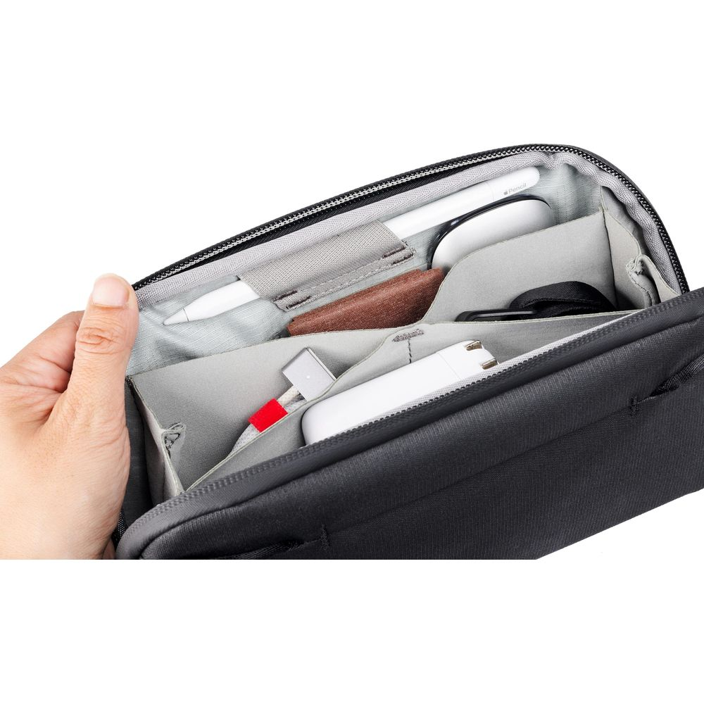 Een hand opent een zwarte tas met pennen, kabels en een witte oplaadadapter erin.