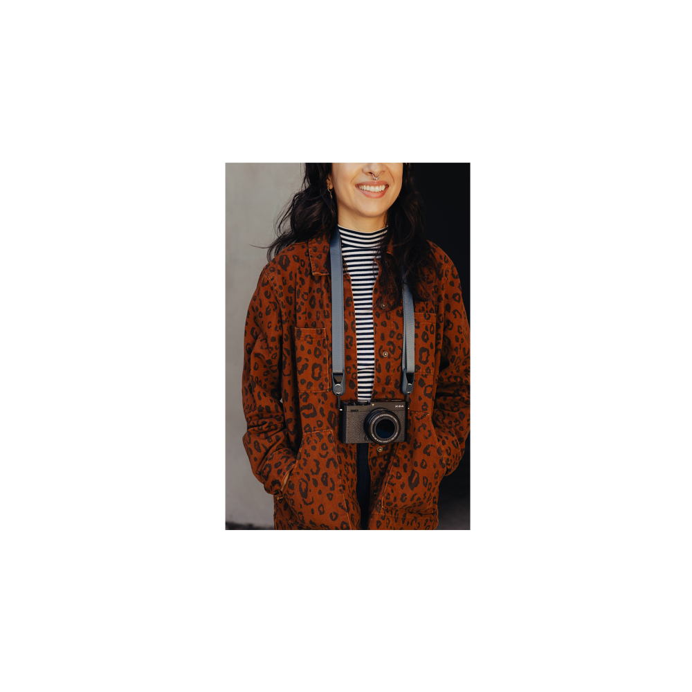 Vrouw in luipaardprint jas met camera om de nek gedragen.