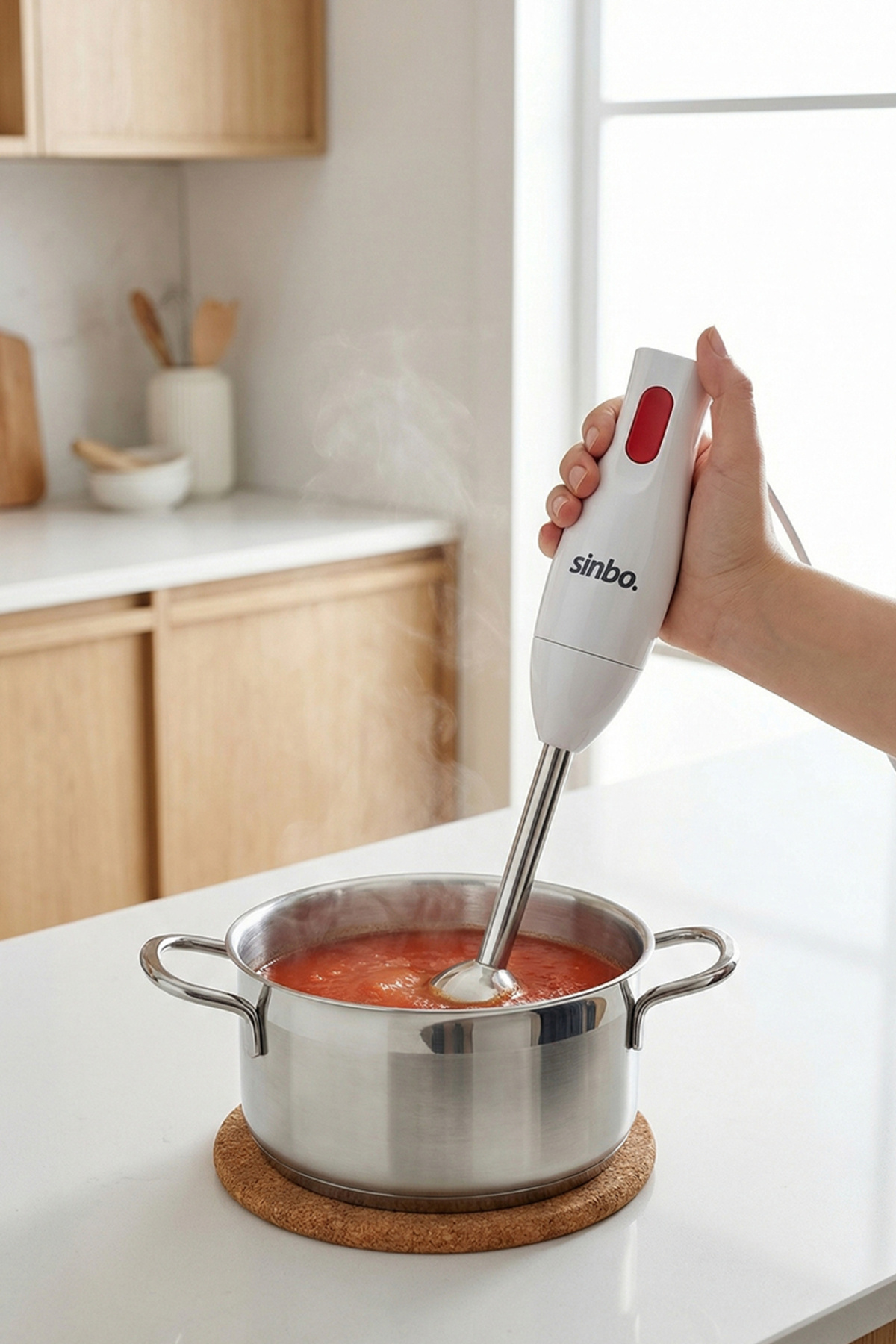 Bir el, kırmızı çorba dolu tencerenin üzerinde beyaz bir el blender tutuyor.