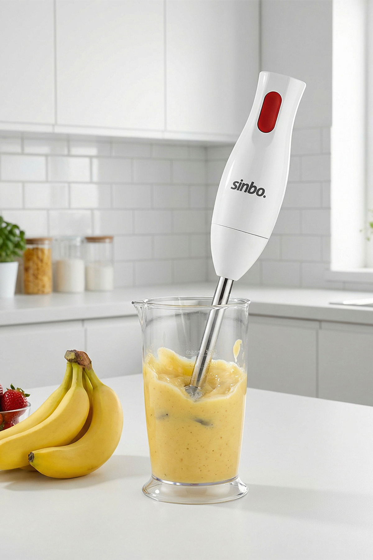 Kırmızı düğmeli beyaz el blenderı cam bardakta muzları karıştırıyor.