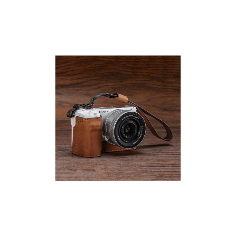 A white Sony camera with a brown leather case on wood.