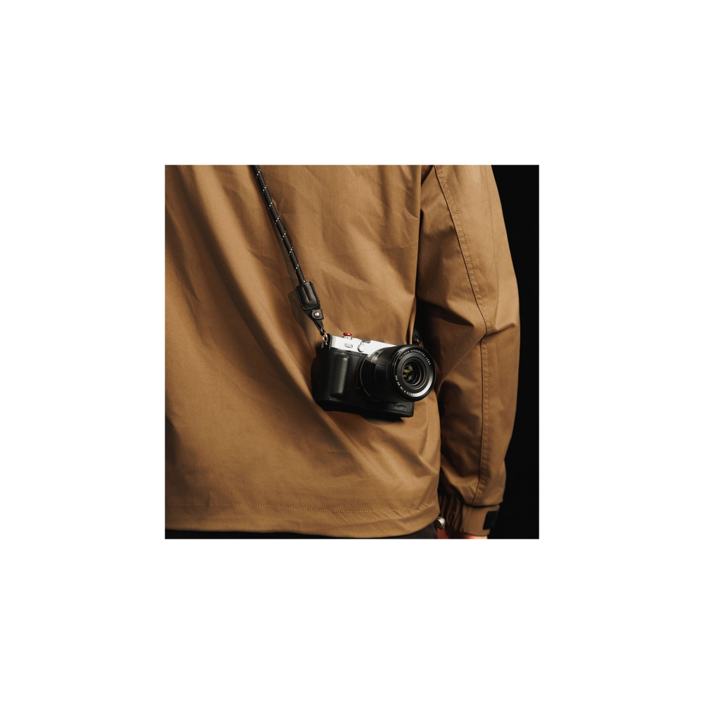 A silver camera with a black grip hangs on a brown strap over a brown jacket.