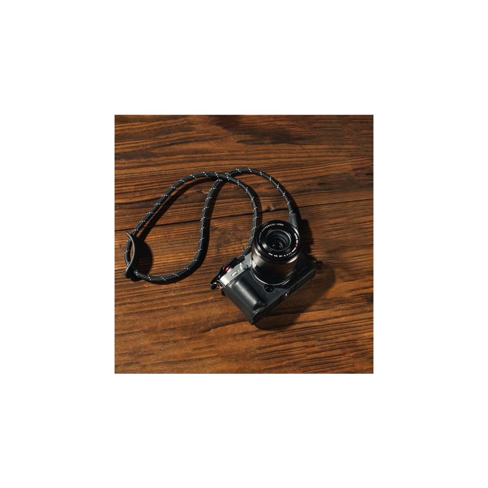 A black camera with a patterned strap rests on a wooden table.