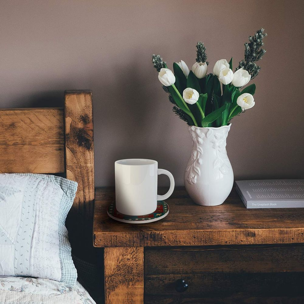A white mug sits on a coaster next to a vase of white tulips.