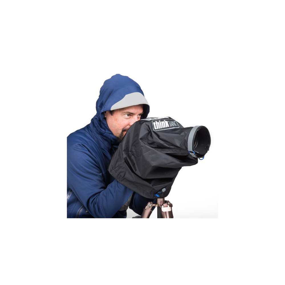 Man in blue hooded jacket holding a camera with a rain cover on a tripod.