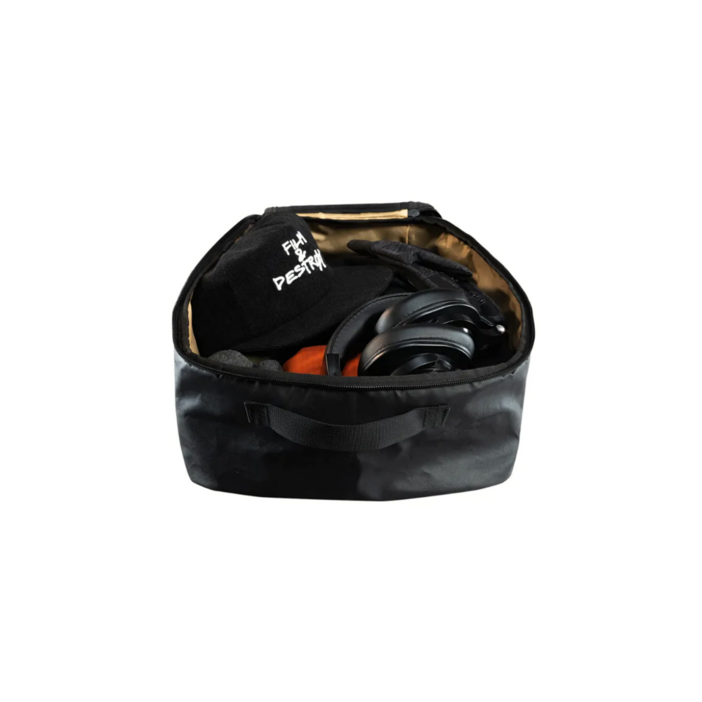 A black bag contains headphones, a black cap with white print, and an orange item.