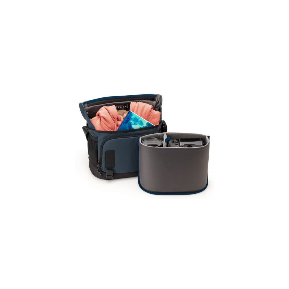 A dark blue camera bag with an insert holding a camera and lenses. Clothes and book in bag.