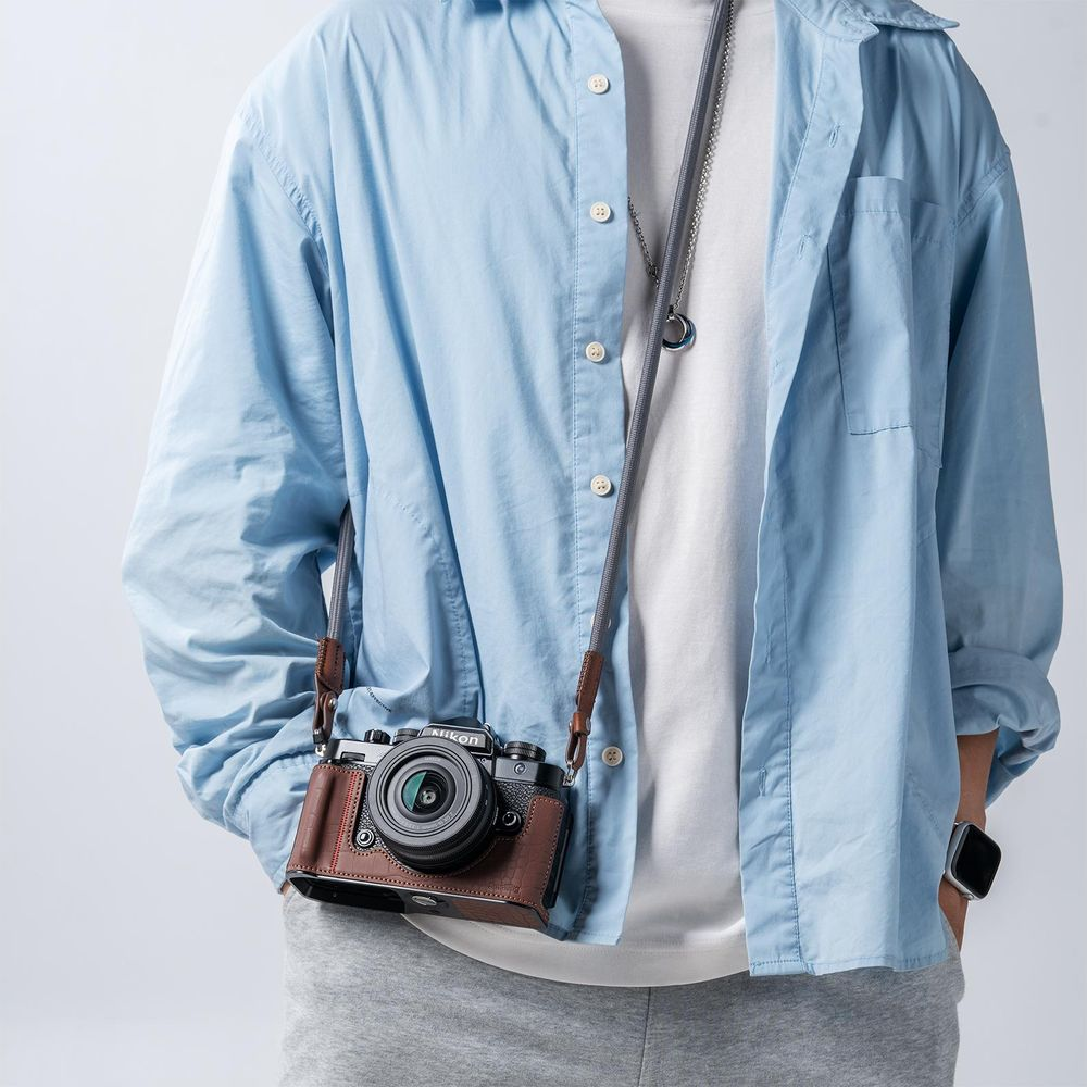 Person wearing a light blue shirt, white t-shirt, and grey pants, with a brown camera.
