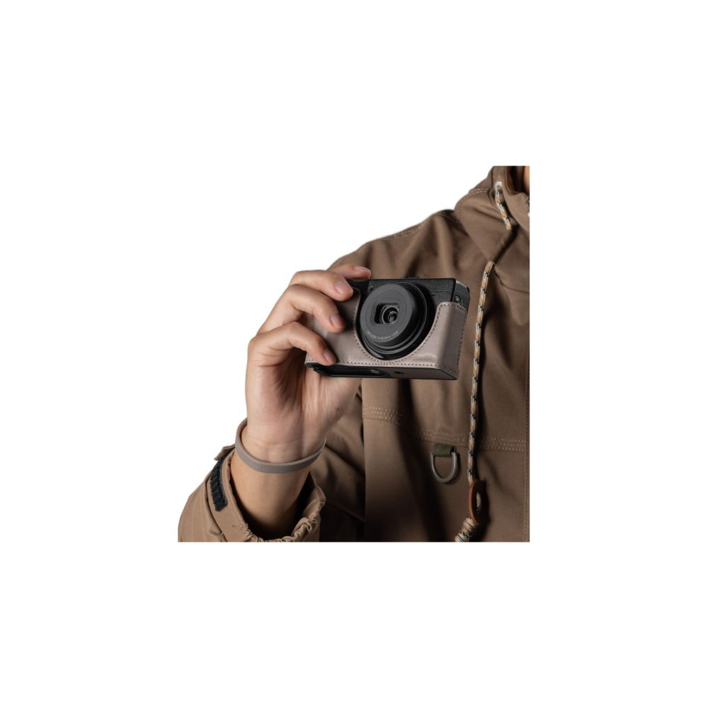 A hand holds a gray camera with a brown jacket in the background.