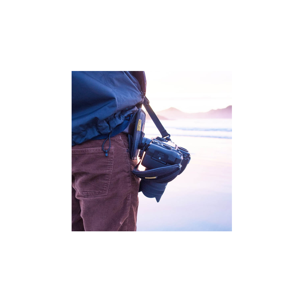 Man met camera op strand, camera aan heup geklemd, zachte zonsondergangslucht.