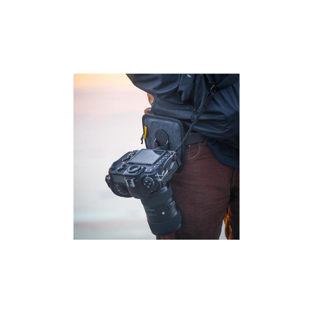 Een fotograaf met een camera op de heup die een bruine corduroy broek draagt.