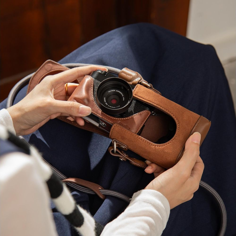 A person holds a brown leather camera case over a camera on their lap.