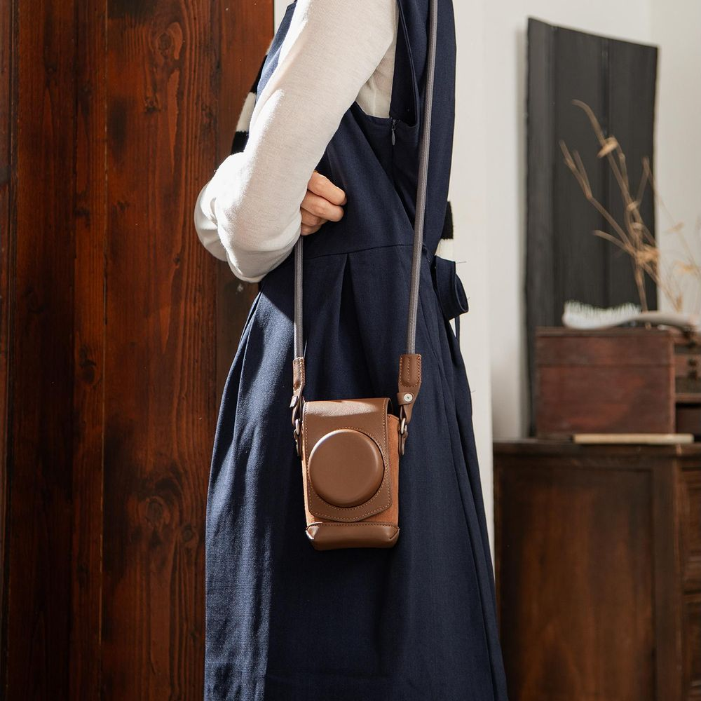 A person wears a dark blue dress and a brown leather camera case hangs from a strap.