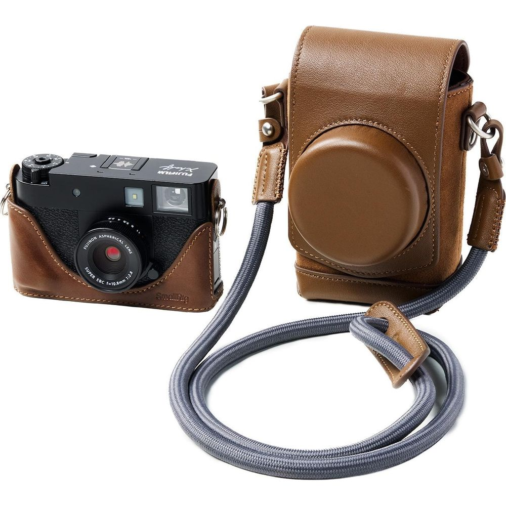 A black camera in a brown leather case with a gray strap on a white background.