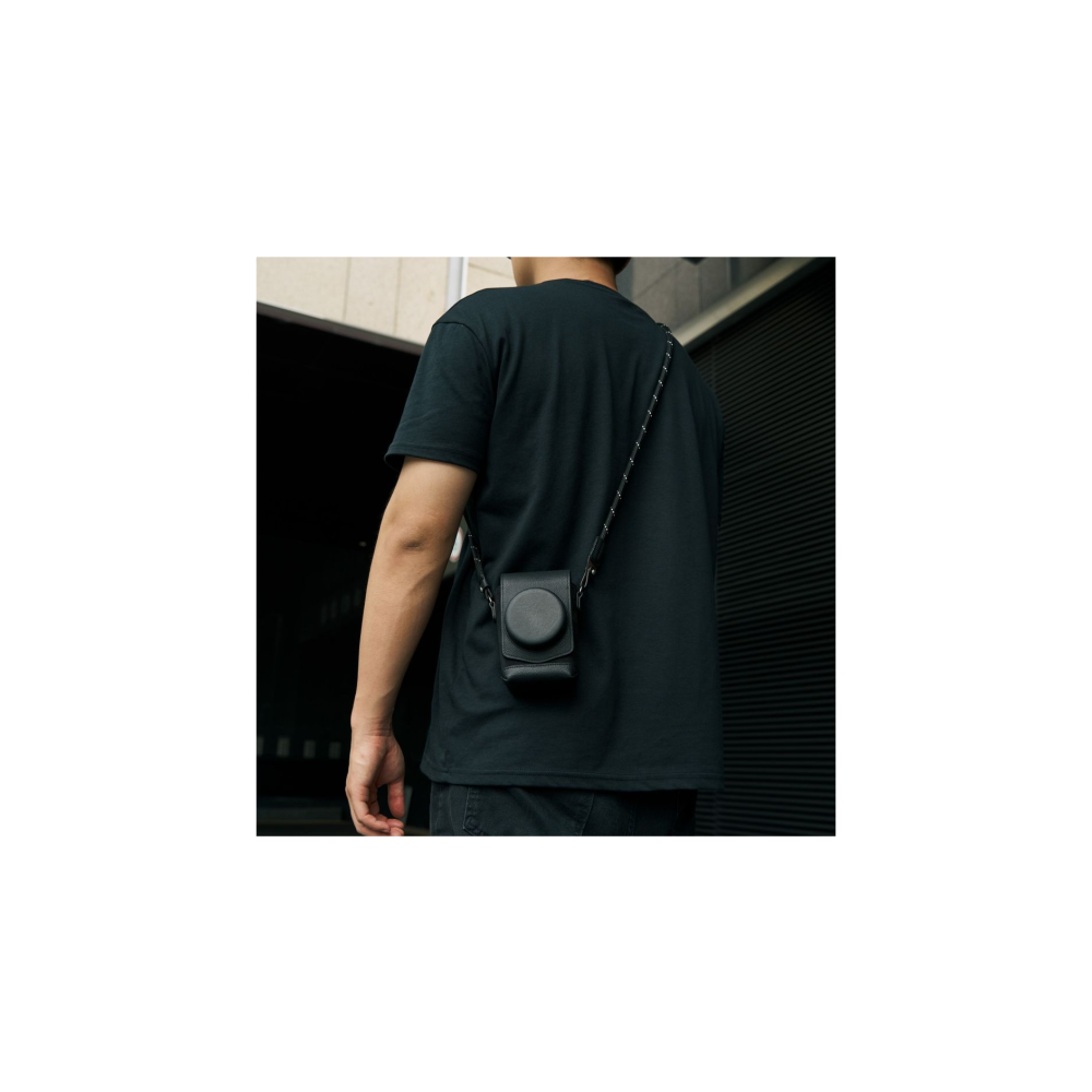 Man met zwarte cameratas om nek, zwart t-shirt, donkere achtergrond.
