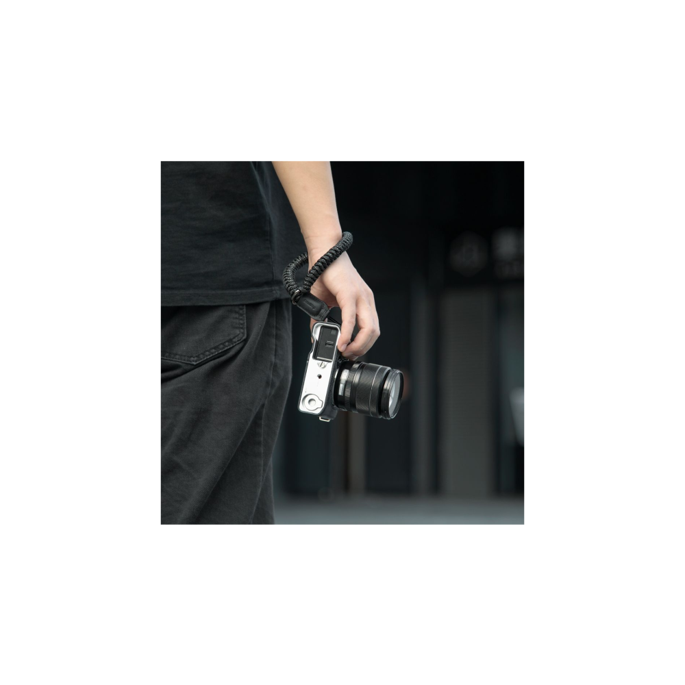 A hand holds a silver camera with a black lens, wrist secured by a black strap.