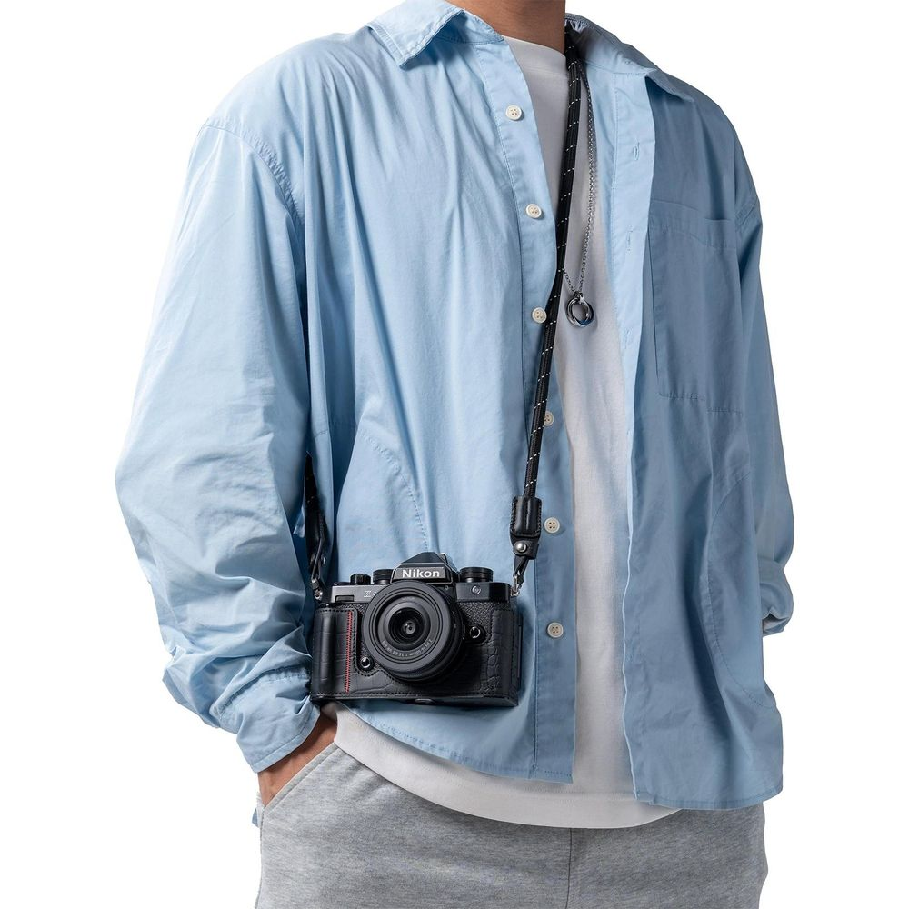 A person in a light blue shirt and grey pants wears a black Nikon camera.