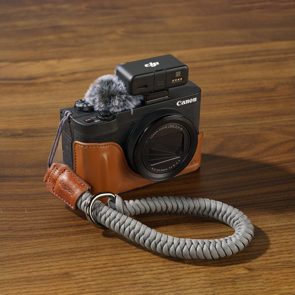 Black Canon camera with microphone and brown leather case, on a wooden surface.