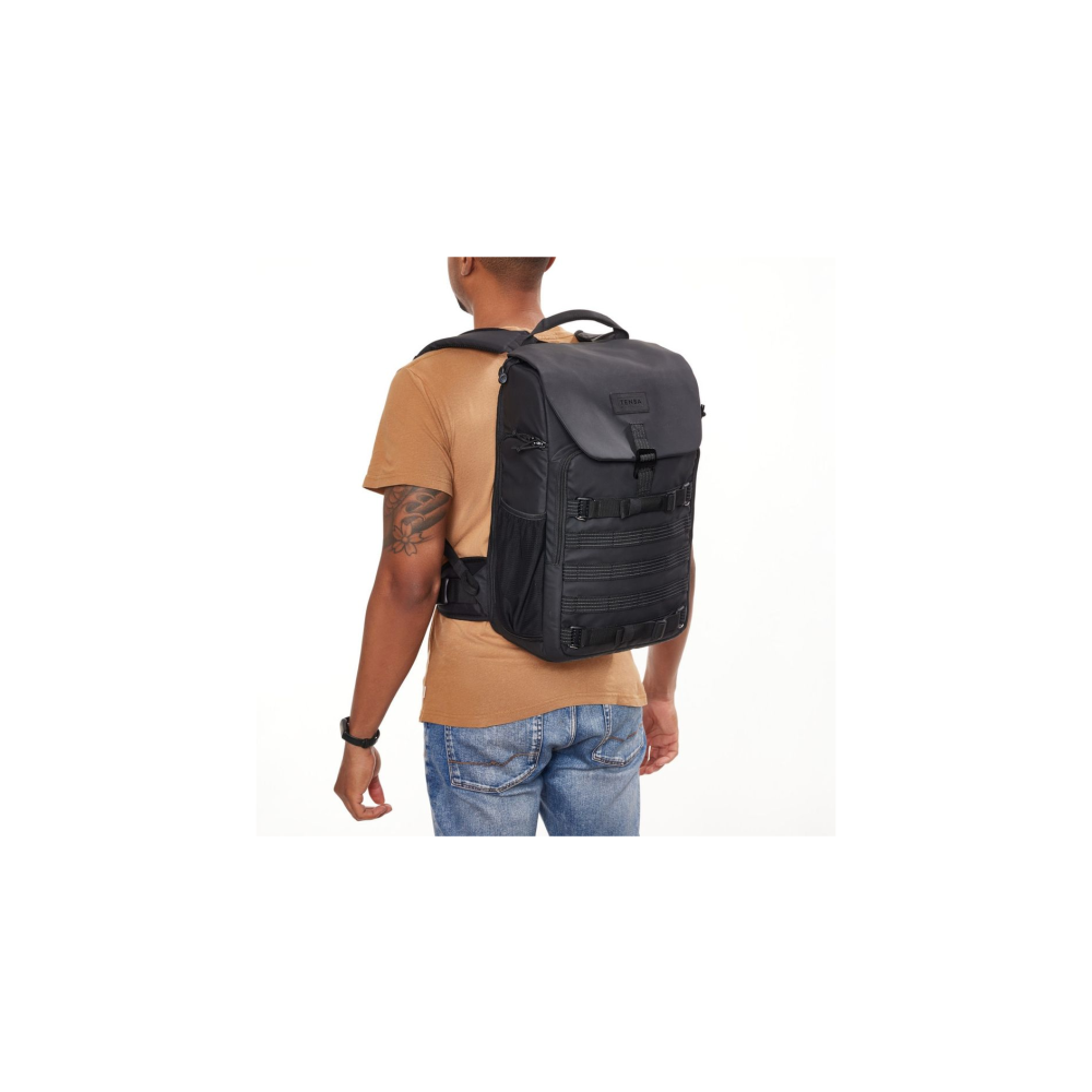 A man wears a black backpack with a brown t-shirt and jeans.