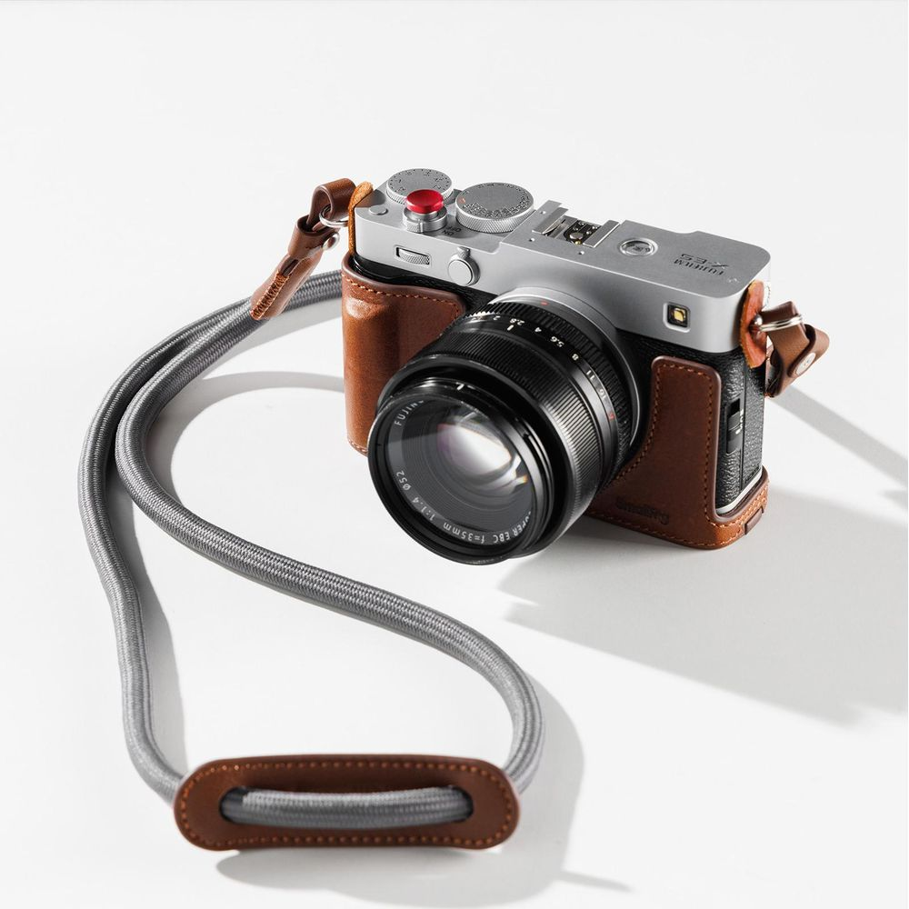 Zilveren camera met bruin lederen hoes en grijze riem op witte achtergrond.