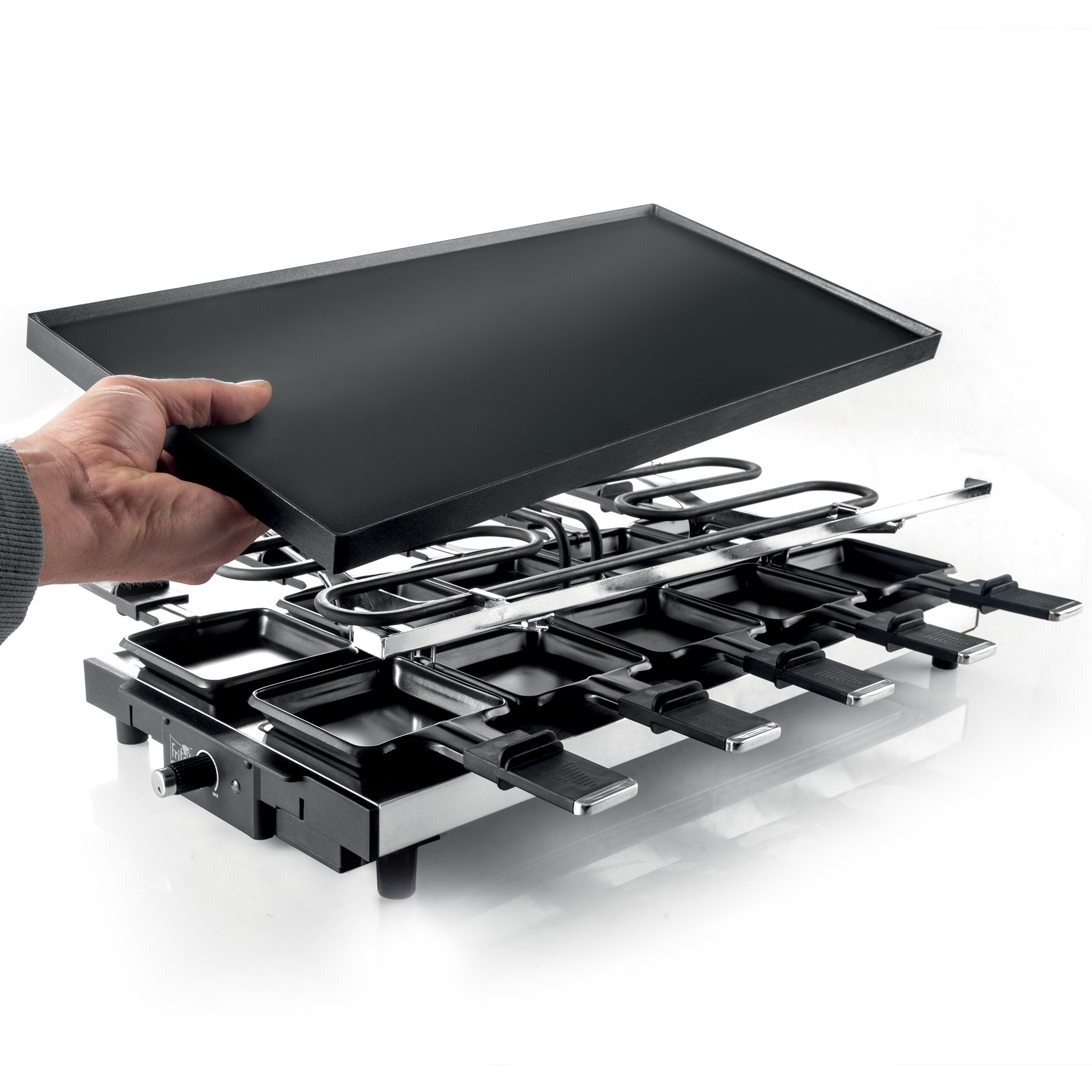 Hand places black grill plate onto raclette grill with many small pans.