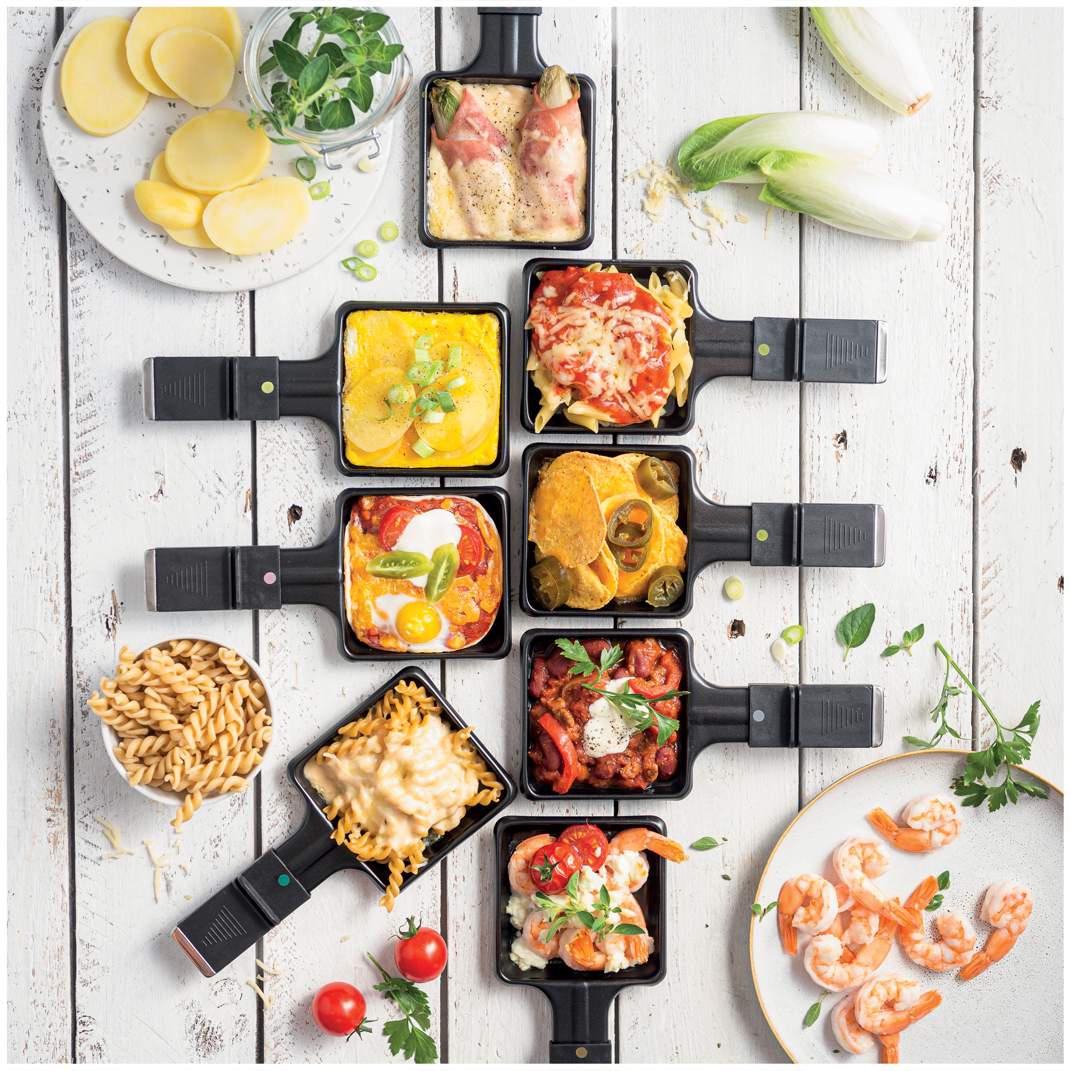 Raclette pans with potatoes, pasta, shrimp, chili con carne, and salad.