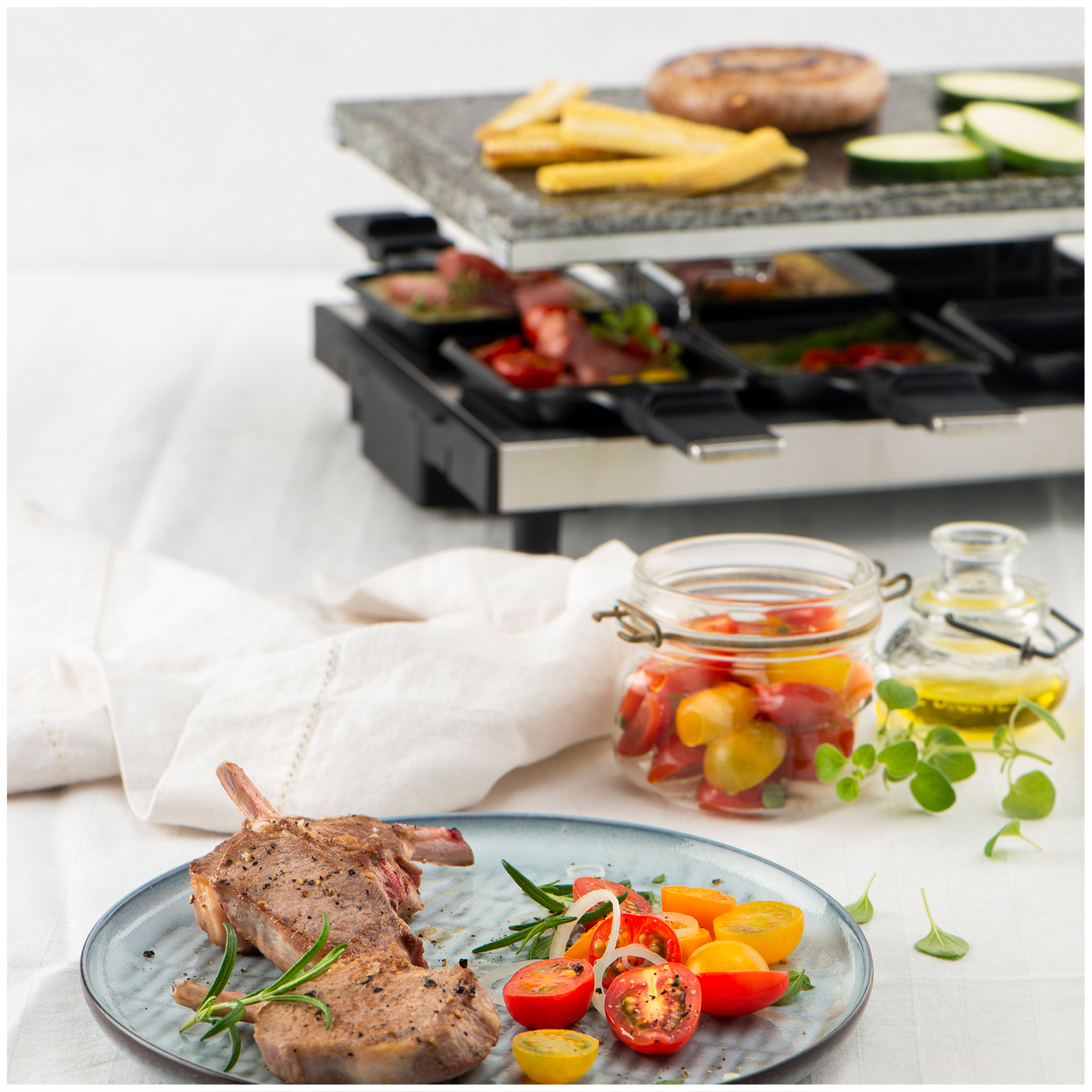 Grilled lamb chops with tomatoes and herbs on a plate, raclette grill in background.
