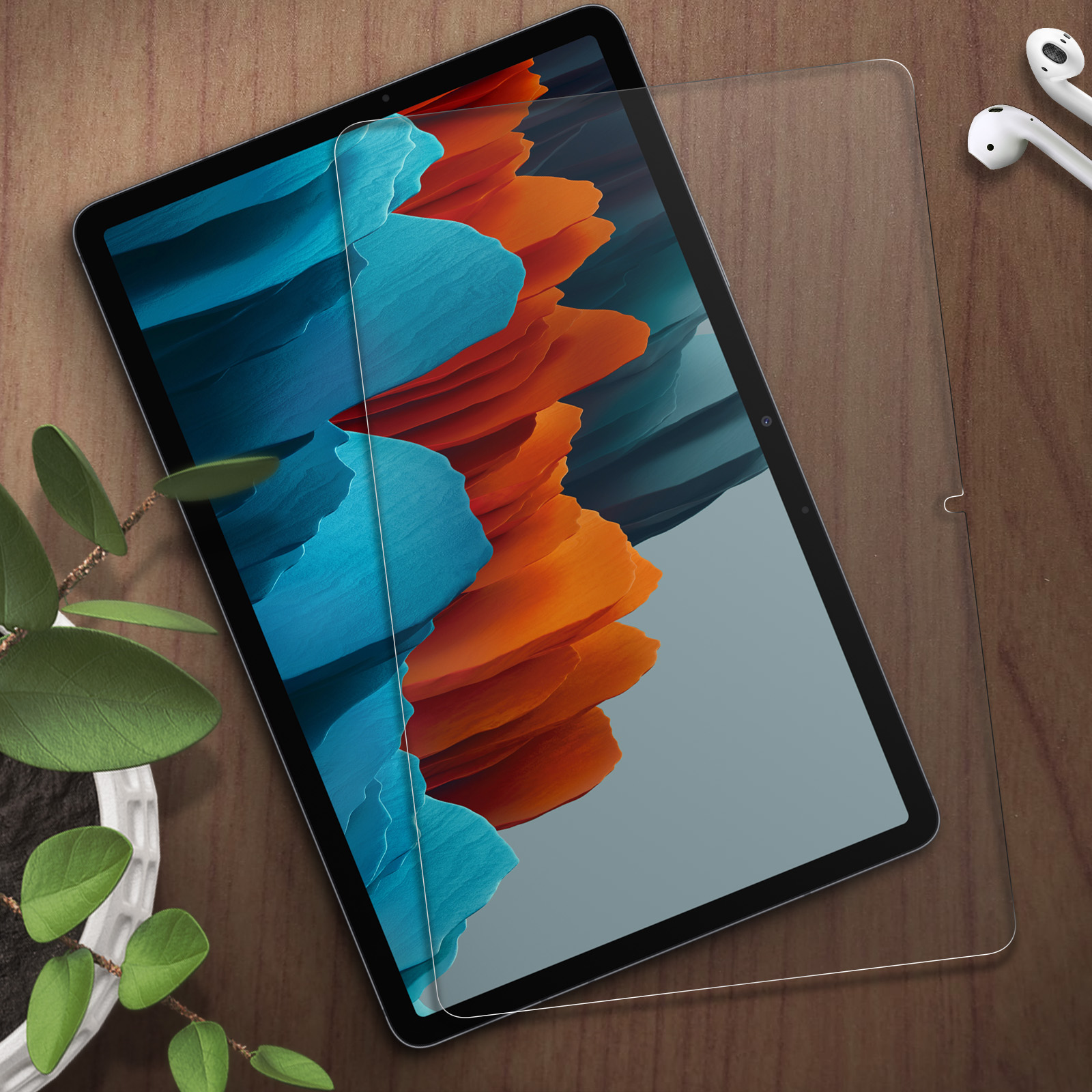 Een tablet met een blauw en oranje achtergrond ligt op een houten tafel. Oordopjes liggen ernaast.