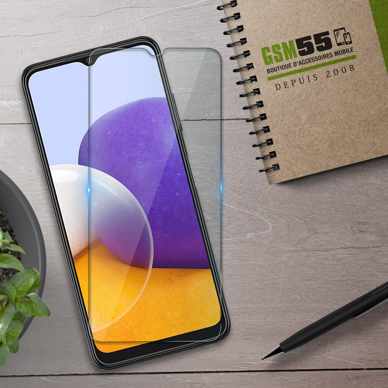 Een smartphone-schermprotector ligt op een houten tafel naast een notitieboek.