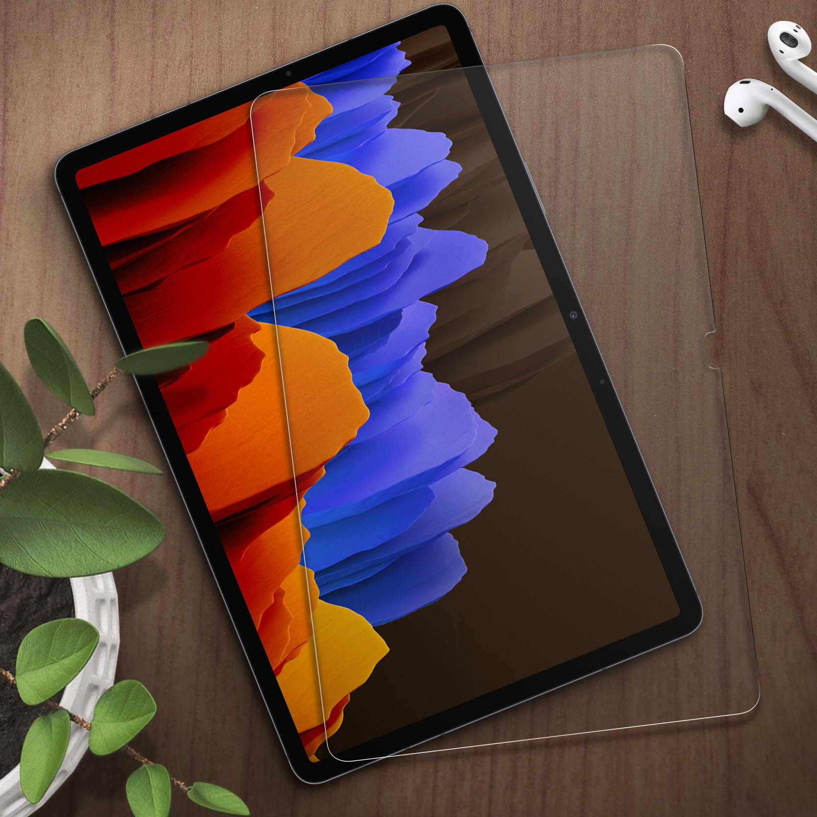 Un tablet con sfondo colorato, vicino a auricolari e una pianta.
