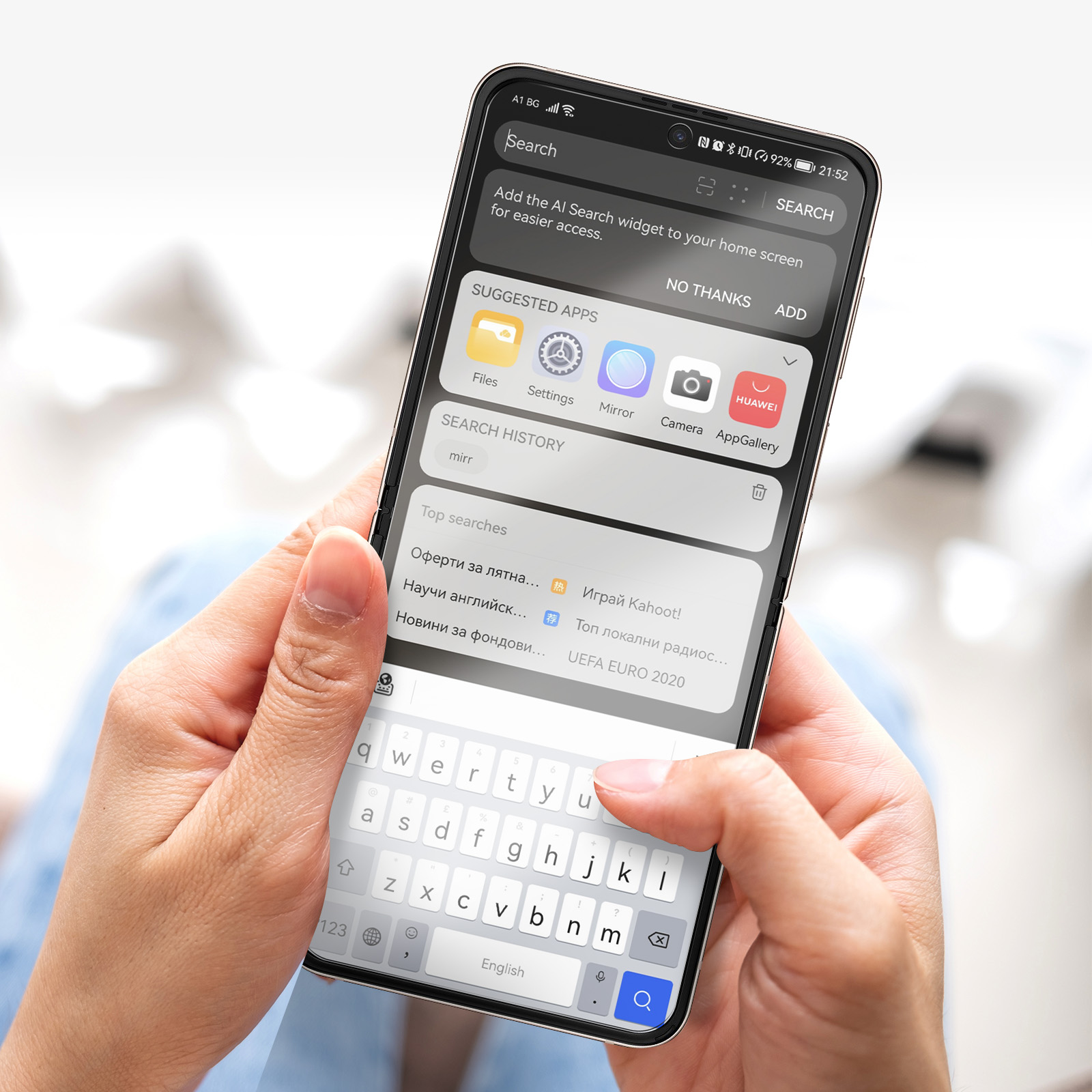 Gros plan de mains tenant un smartphone affichant une barre de recherche, des apps suggérées et un clavier.