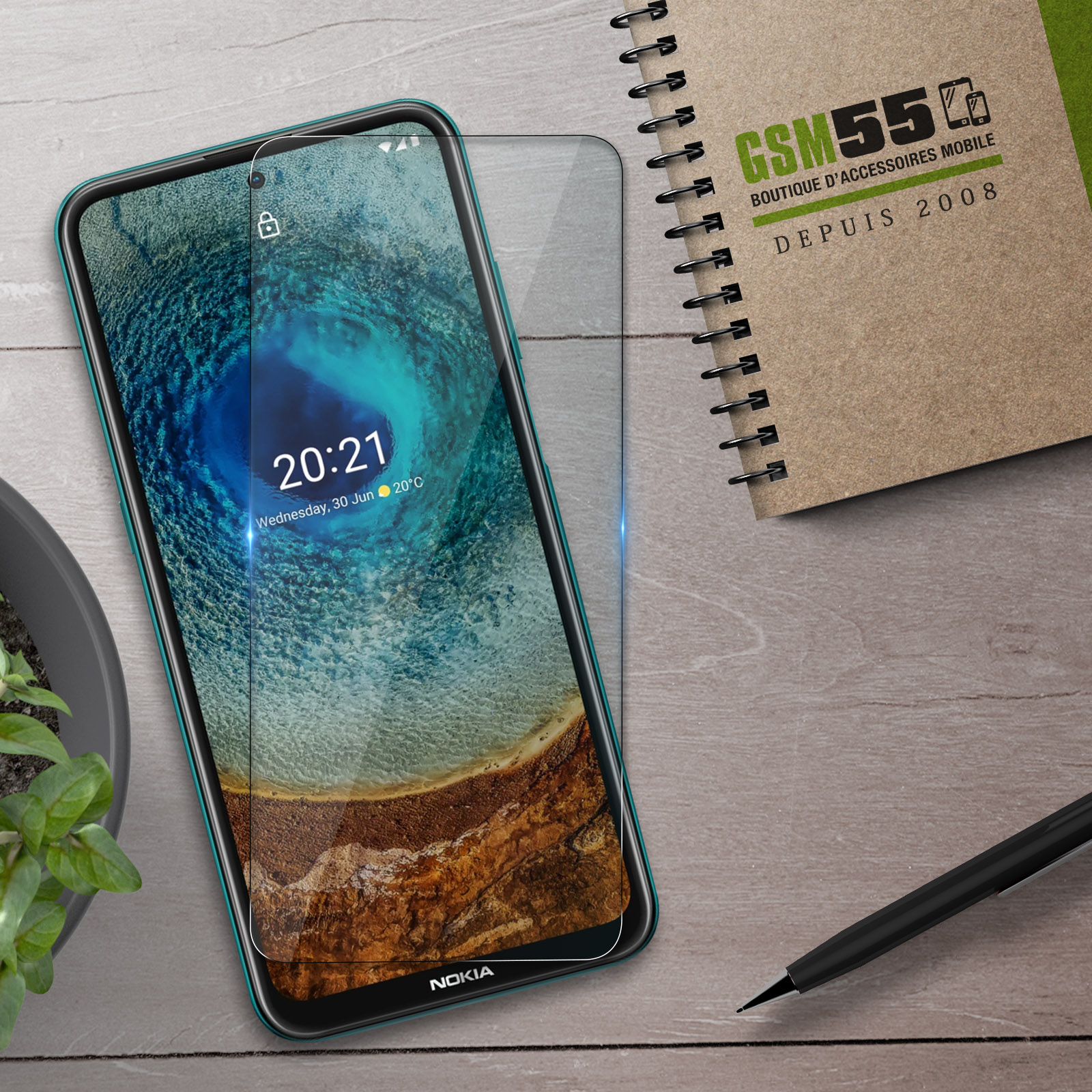 Smartphone met schermprotector naast notitieboek en pen op houten tafel.