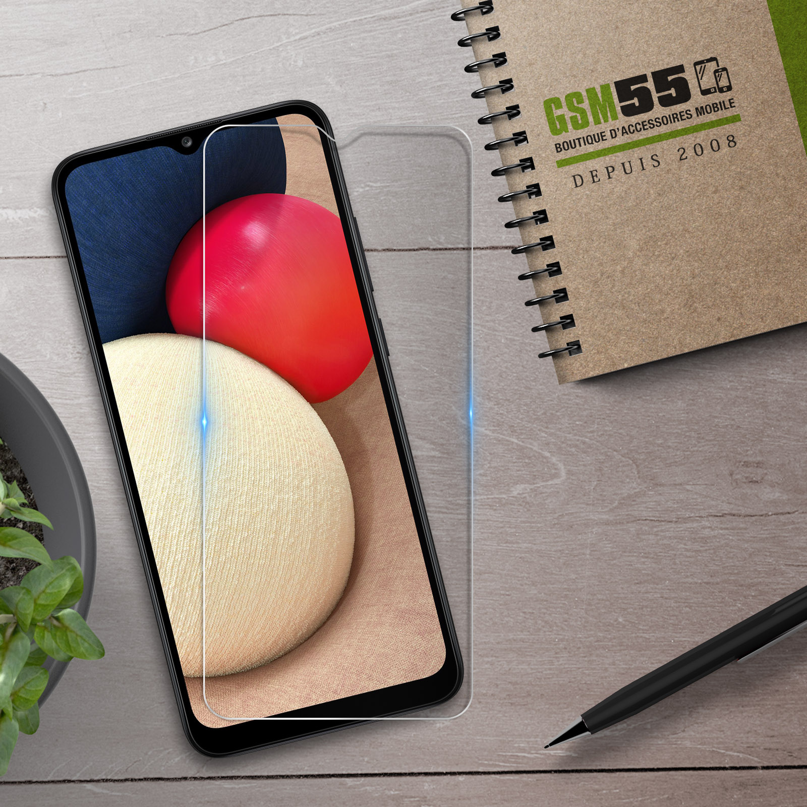 Een smartphone met screenprotector, notitieboek en pen op een houten achtergrond.