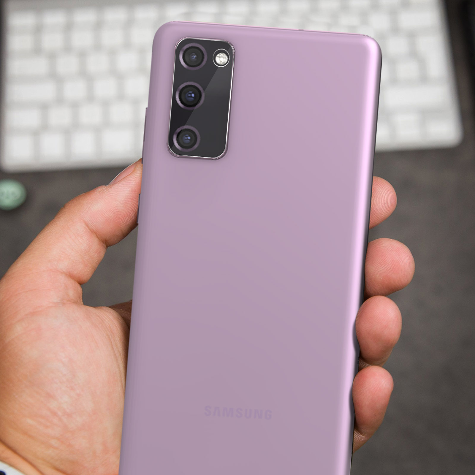 Une main tient un téléphone Samsung violet devant un clavier.