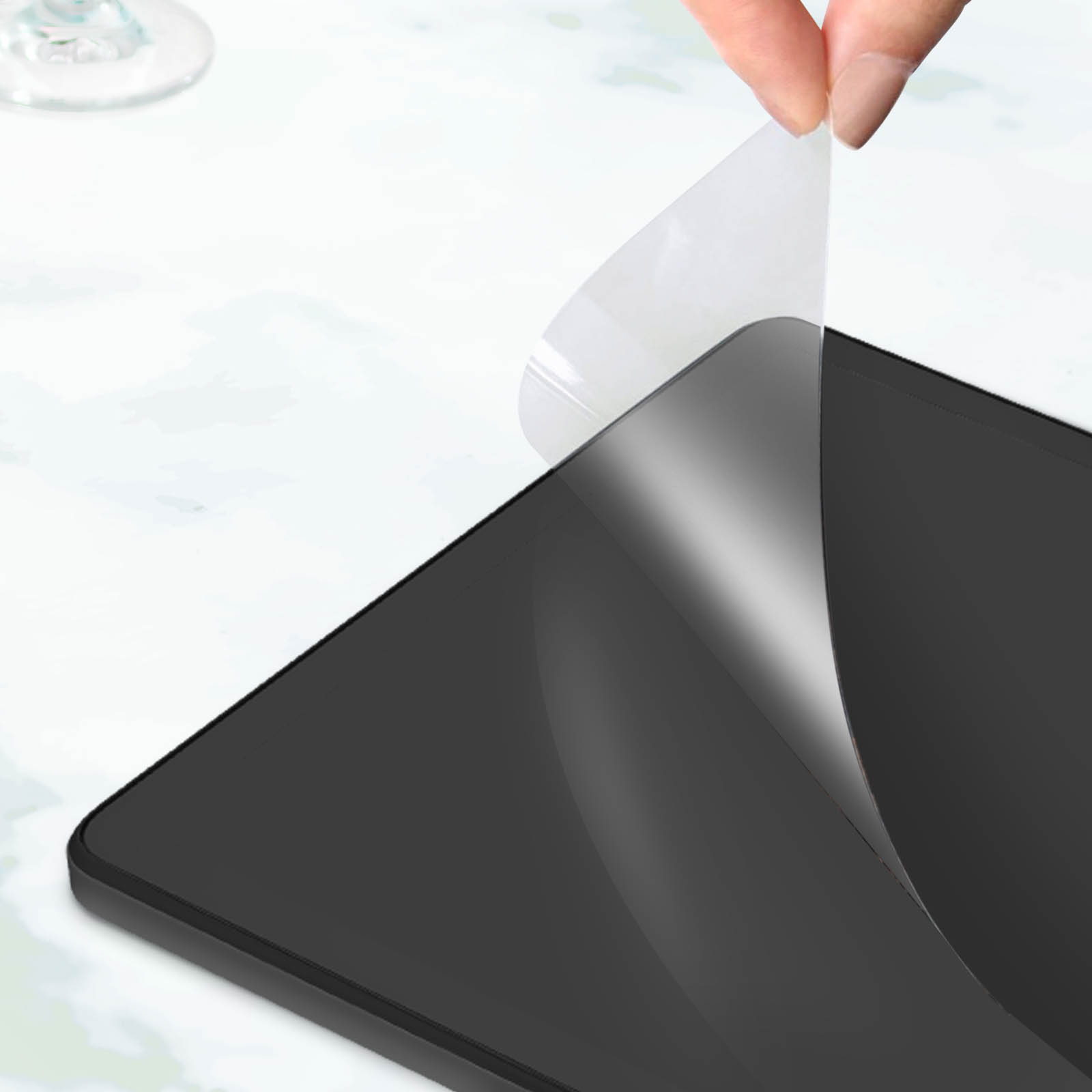 Una mano despega una película protectora transparente de la pantalla de un dispositivo oscuro.