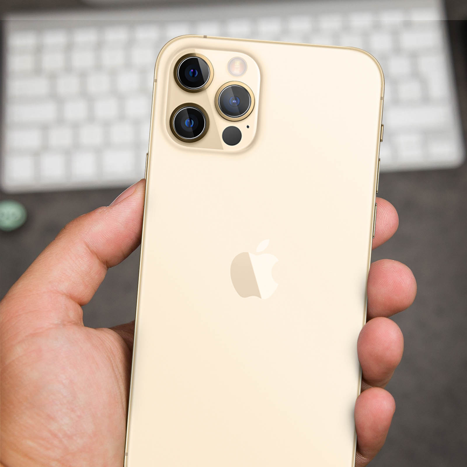 Een gouden iPhone met drie camera's in de hand, toetsenbord op de achtergrond.