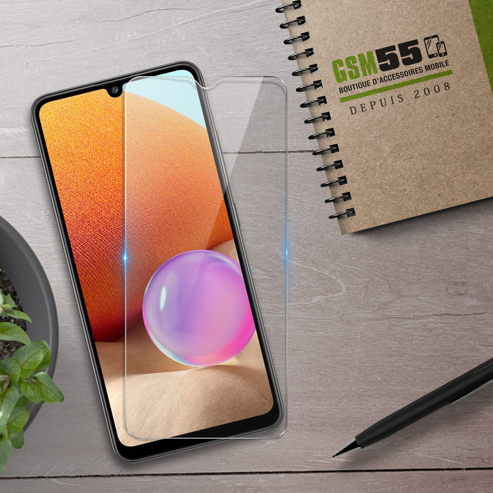 Smartphone met screenprotector, notitieboek en pen op houten tafel.