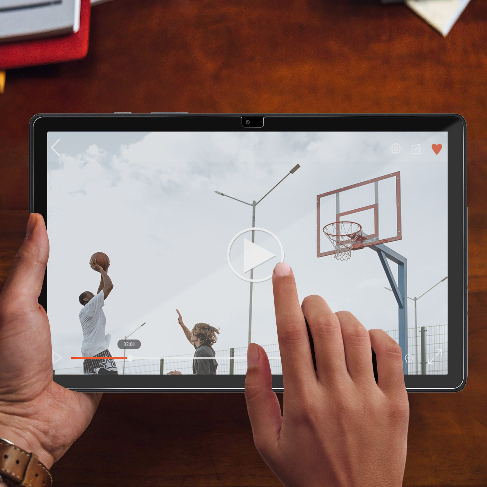 Een tablet toont een basketbalwedstrijd buiten, een vinger tikt de play-knop aan.