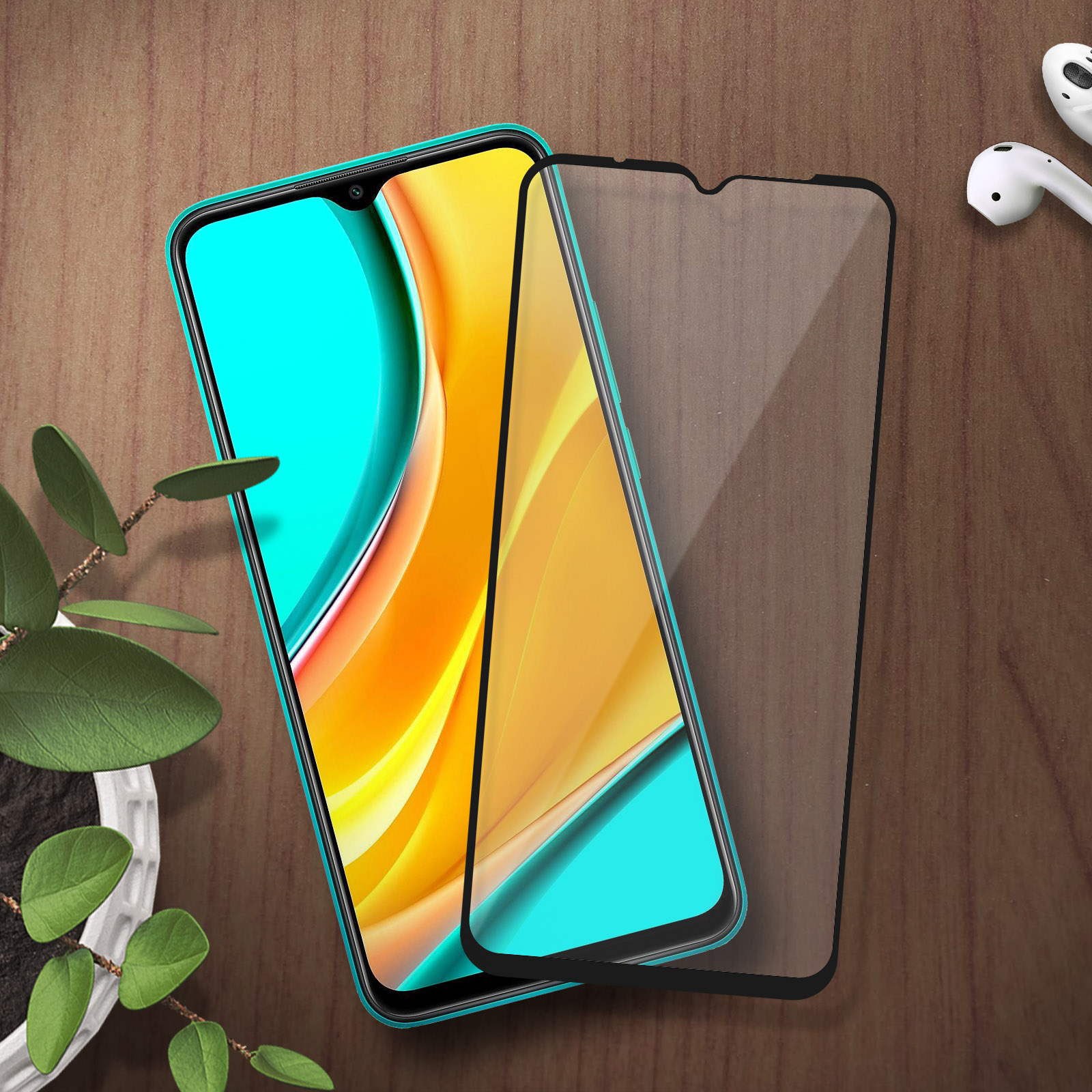 Un smartphone avec un boîtier bleu et un protecteur d'écran sur une table en bois près d'une plante en pot et d'écouteurs.