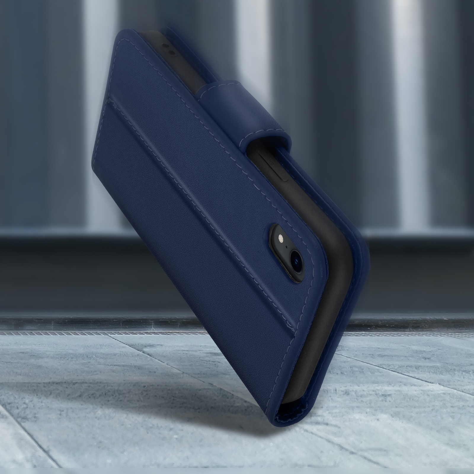 Custodia a libro in pelle blu scuro per smartphone con ritagli fotocamera su cemento.