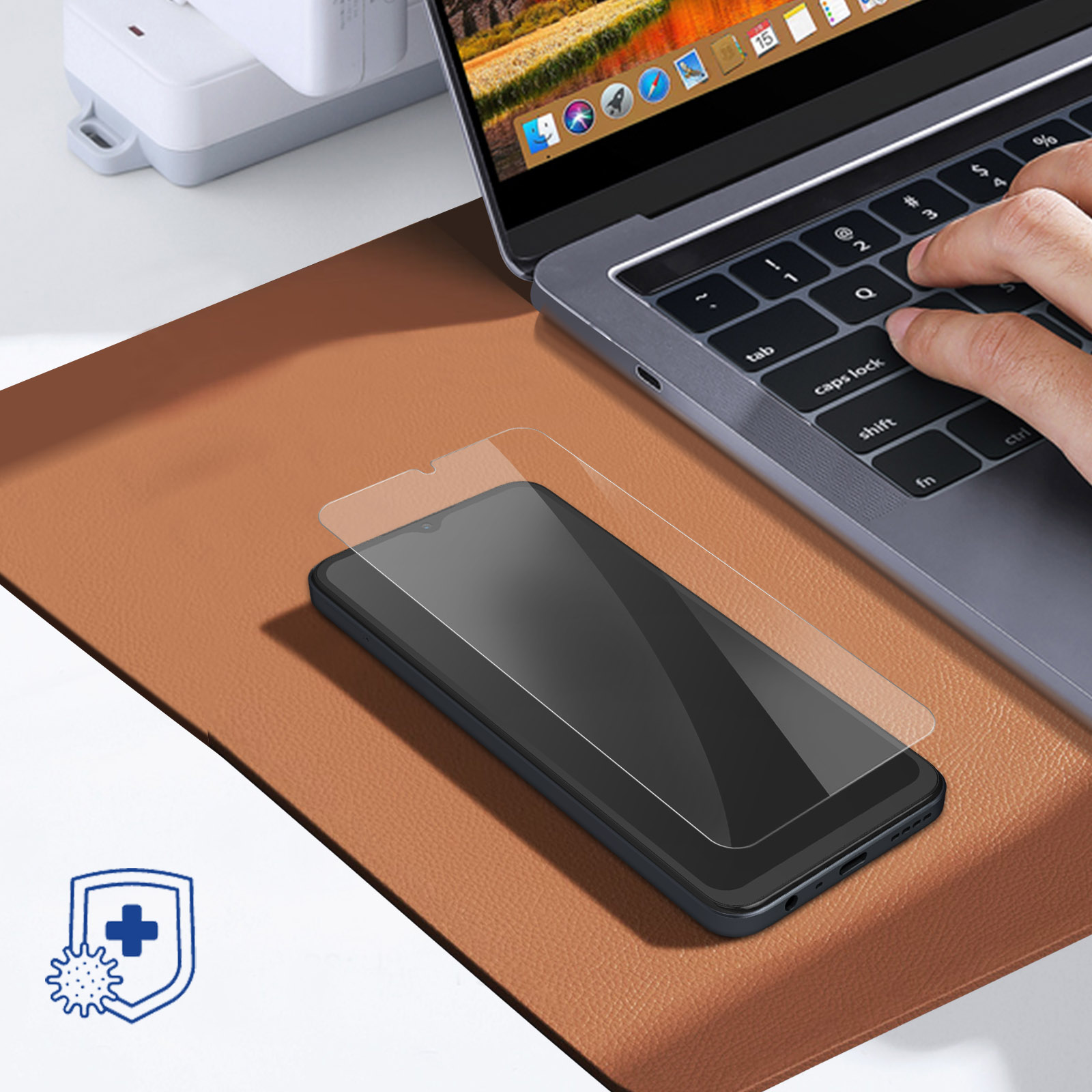 Een smartphone met schermprotector ligt op een bruine mat naast een laptop.