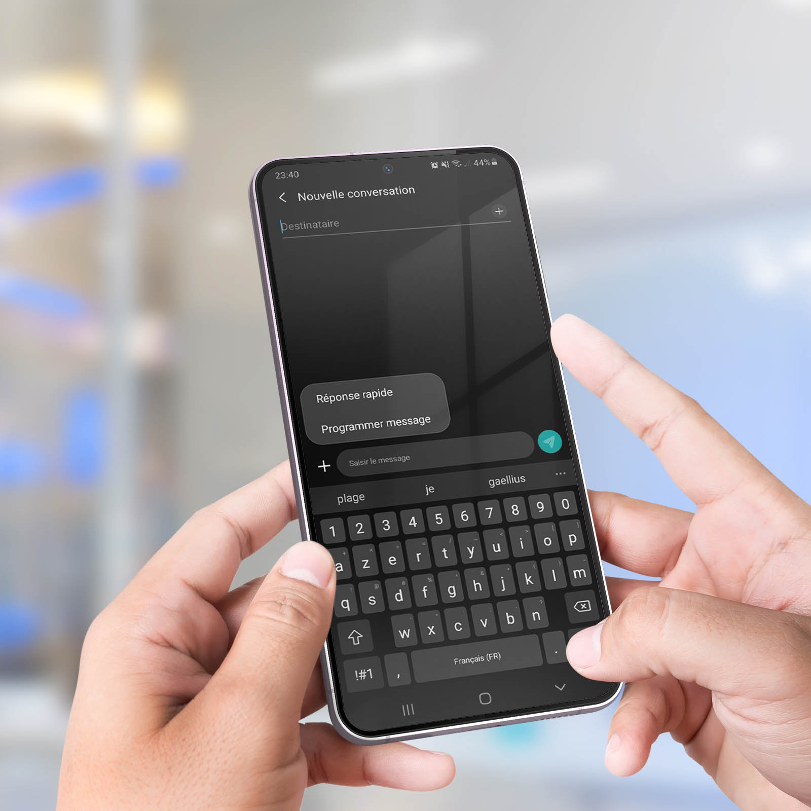 Dłonie trzymają smartfon z klawiaturą i aplikacją do wiadomości. Rozmyte światła w tle.