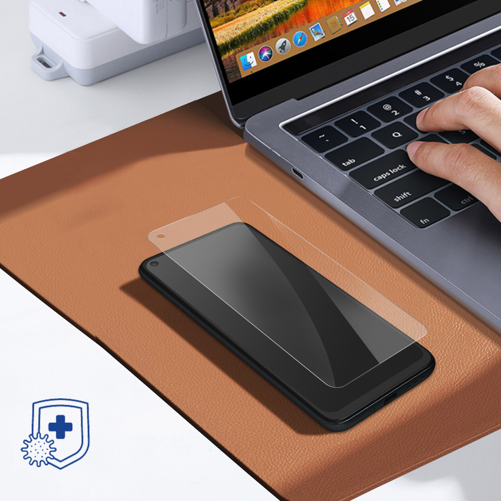 Uno smartphone nero con protezione schermo giace su un tappetino marrone vicino a un laptop.
